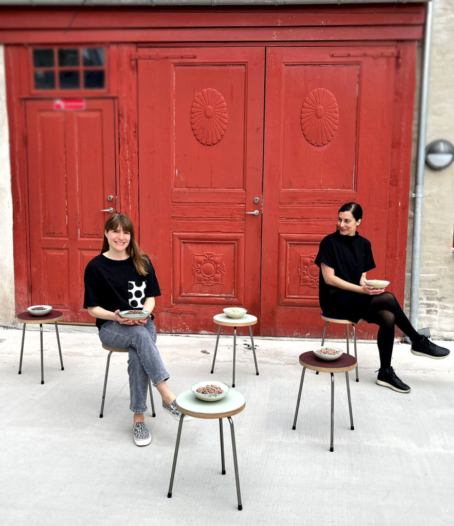Two founders sitting on chairs outside red door.